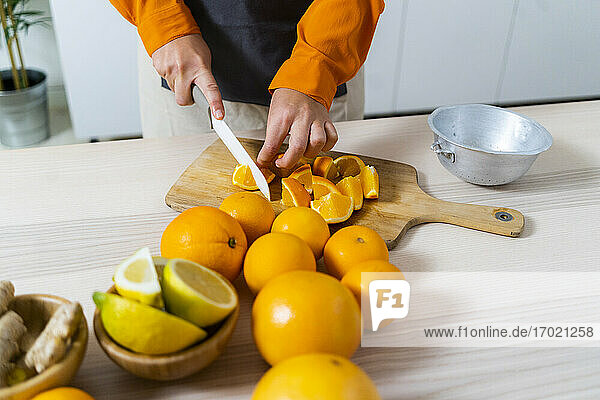 Frau schneidet Orangenfrüchte für die Zubereitung von frischem Saft  während sie in der Küche zu Hause steht