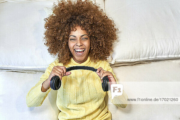 Lachende Frau  die nach der Arbeit im Schlafzimmer mit Kopfhörern spielt