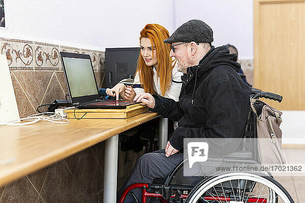 Junge Krankenschwester unterrichtet einen behinderten Mann im Rehabilitationszentrum am Laptop