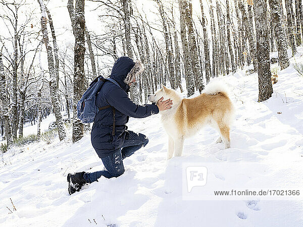 Man kneeling while looking at dog on snow in forest