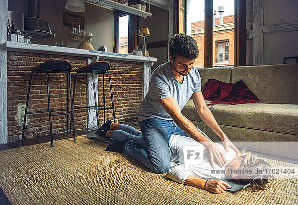 Junger Mann massiert Freundin auf Teppich im Wohnzimmer zu Hause liegend