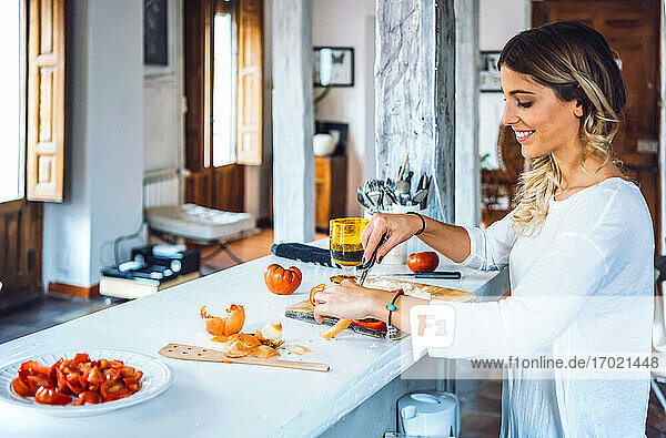 Beautiful young woman smiling and chopping vegetables for dinner