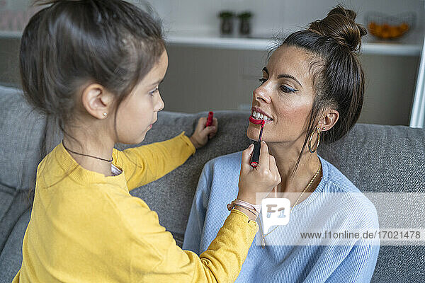 Tochter appliziert roten Lippenstift auf Mutter im Wohnzimmer zu Hause