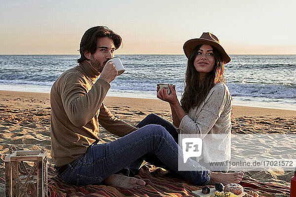 Junges Paar trinkt Kaffee und sitzt zusammen am Strand