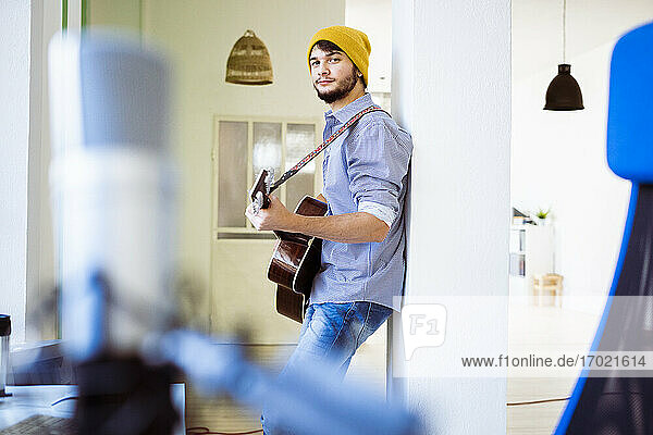 Selbstbewusster Gitarrist spielt Gitarre und lehnt sich im Studio an eine Säule