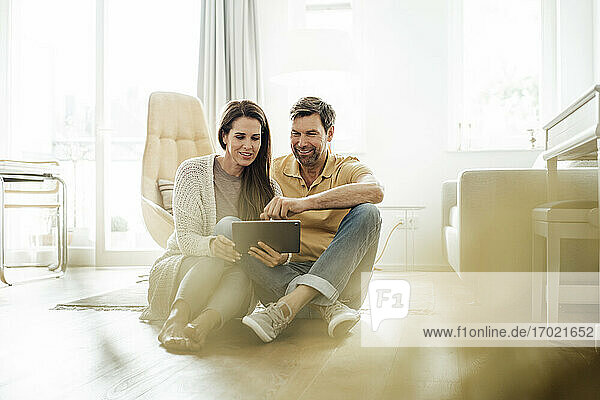 Smiling mature couple using digital tablet together while sitting on floor at home