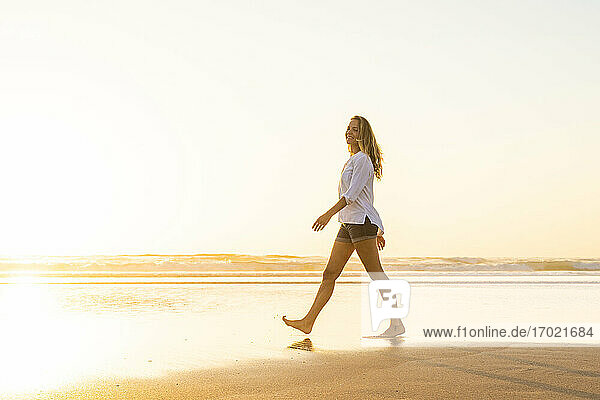 Glückliche Frau  die bei Sonnenuntergang am Strand spazieren geht