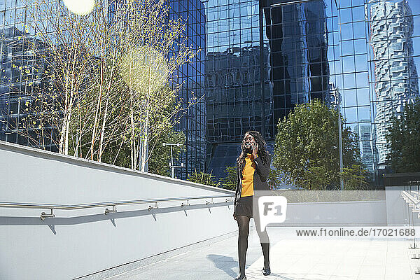 Weibliche Fachkraft am Telefon zu Fuß gegen Bürogebäude an einem sonnigen Tag