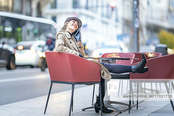 Frau  die in einem Café auf einem Stuhl sitzend mit einem Mobiltelefon spricht