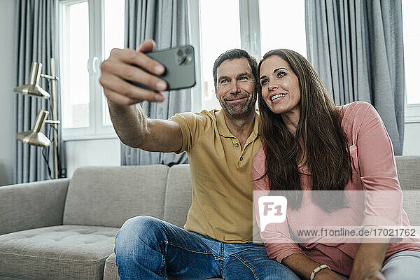 Smiling mature couple taking selfie in apartment