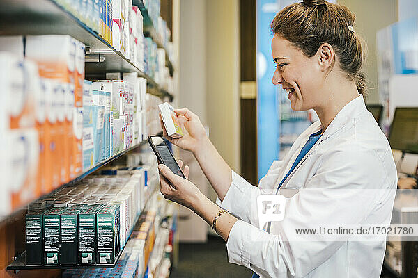 Glückliche Apothekerin mit Smartphone bei der Medikamentenkontrolle in der Apotheke