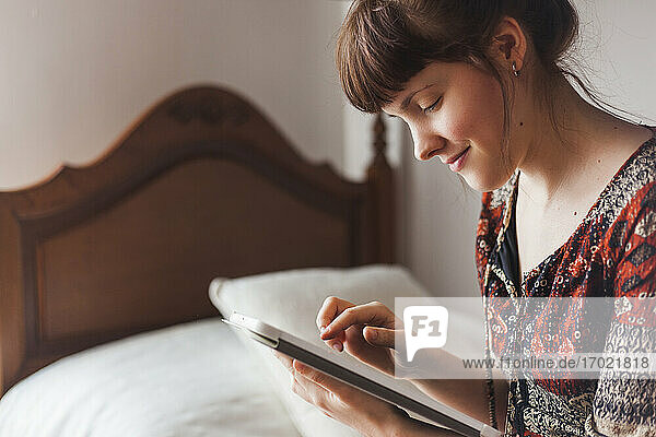Lächelnde Frau  die im Schlafzimmer zu Hause Nachrichten auf ihrem digitalen Tablet sieht