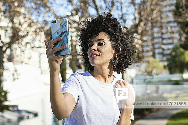 Lächelnde Frau  die ein Selfie mit ihrem Mobiltelefon macht  während sie im Freien steht