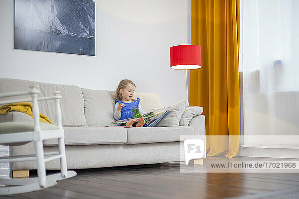 Lächelndes Mädchen  das zu Hause auf dem Sofa sitzt und ein Buch liest