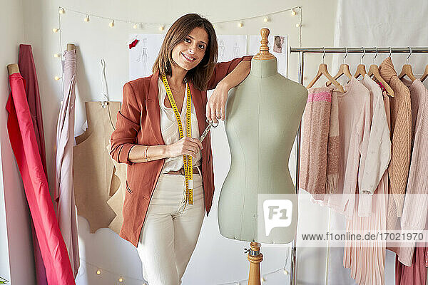 Lächelnde  schöne Modedesignerin  die neben einem Schneidermodell im Atelier steht