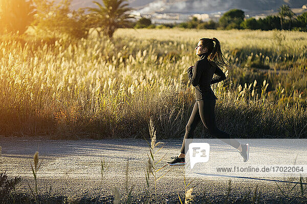 Junge Frau joggt auf dem Fußweg gegen die Landschaft bei Sonnenuntergang