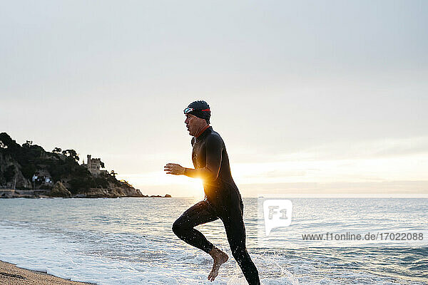 Männlicher Schwimmer verlässt das Wasser nach dem Schwimmen im Meer bei Sonnenuntergang