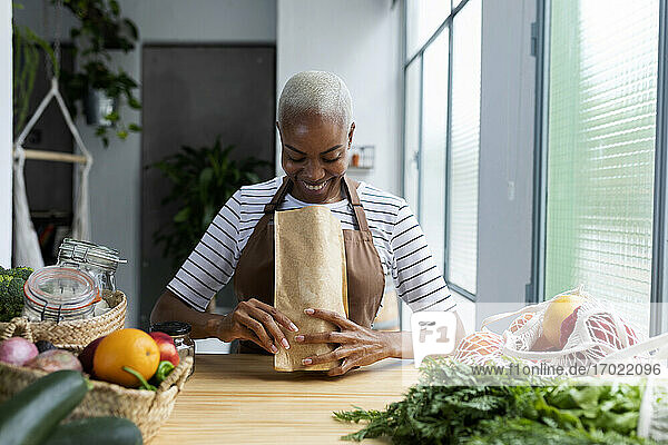 Frau mit Schürze in der Küche  beim Auspacken von frisch gekauftem Bio-Obst und -Gemüse