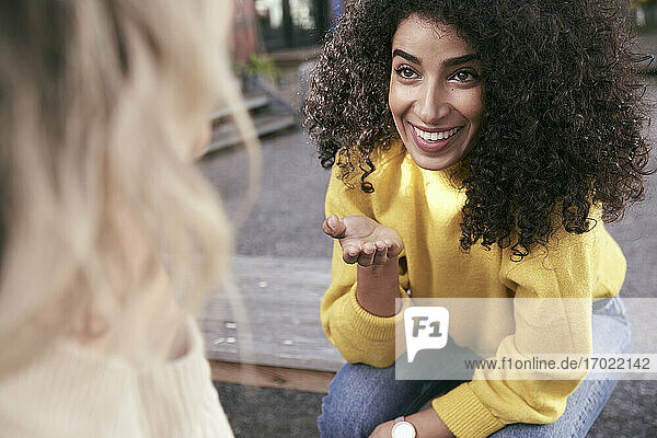 Smiling beautiful woman talking with female friend while sitting on seat