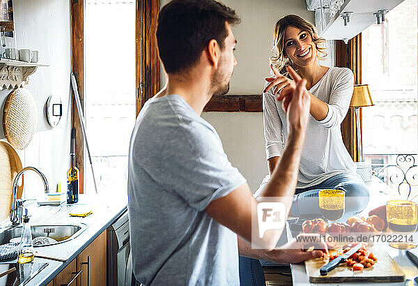Junger Mann bereitet Essen zu und gestikuliert mit Freundin in der Küche zu Hause