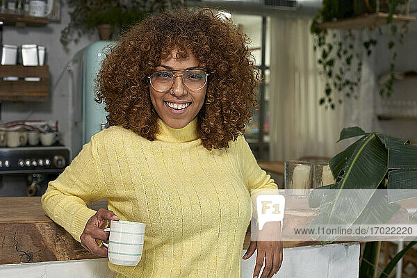 Lächelnde Frau mit Kaffeetasse an der Theke eines Cafés lehnend