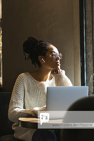 Junge nachdenkliche Frau  die mit ihrem Laptop in einem Café sitzt und wegschaut