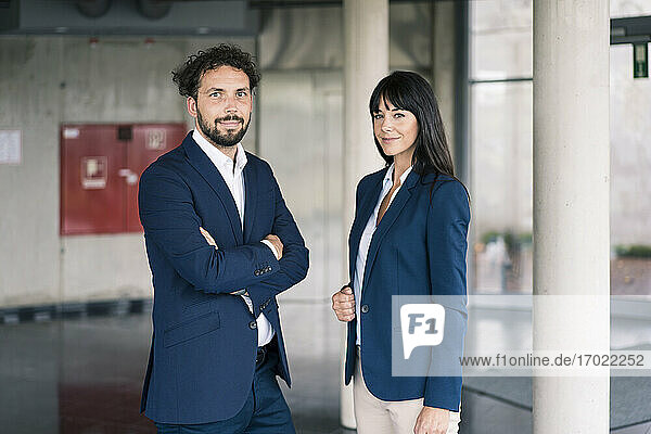Male entrepreneur with arms crossed standing by female colleague in office lobby