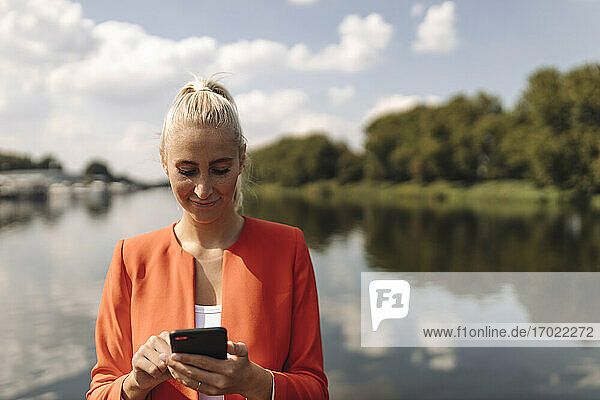 Female entrepreneur using smart phone against lake on sunny day