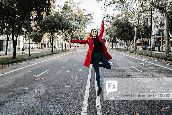 Junge Frau tanzt mit erhobenen Armen und springt auf die Straße