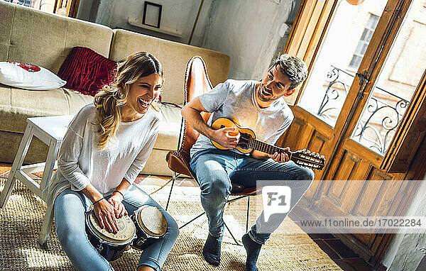 Glückliches junges Paar spielt Duett mit Schlagzeug und Gitarre im Wohnzimmer zu Hause