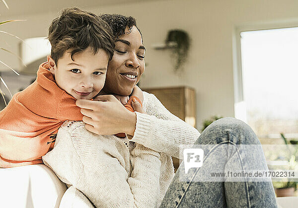 Smiling boy embracing mother while playing at home
