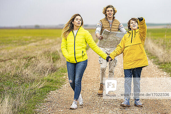 Three siblings hiking with map along dirt road