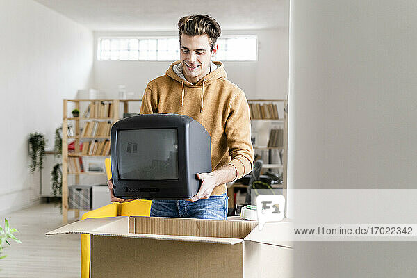 Junger Mann verpackt Fernsehgerät in Karton beim Umzug in eine neue Wohnung