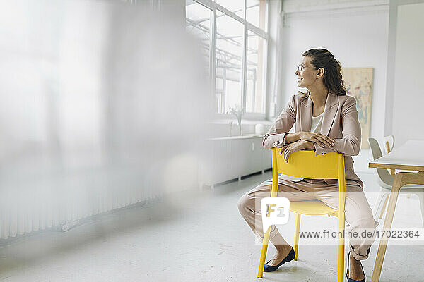 Lächelnde Geschäftsfrau sitzt auf einem Stuhl in einem leeren Büro