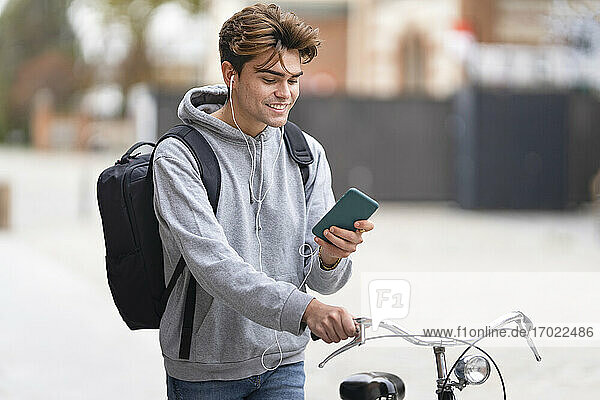 Lächelnder junger Mann  der ein Mobiltelefon benutzt  während er in der Stadt Fahrrad fährt