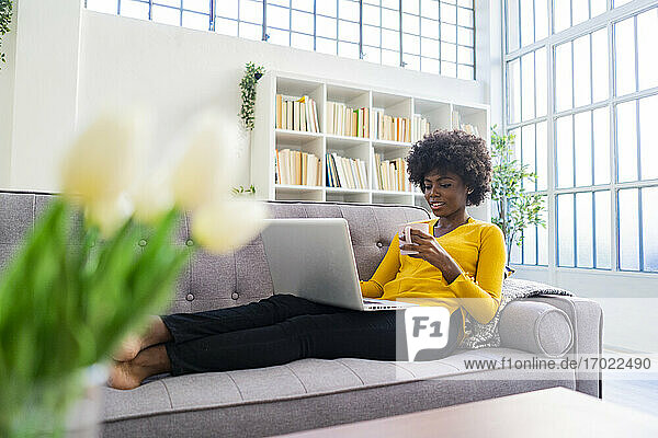 Woman drinking coffee while working on laptop at home