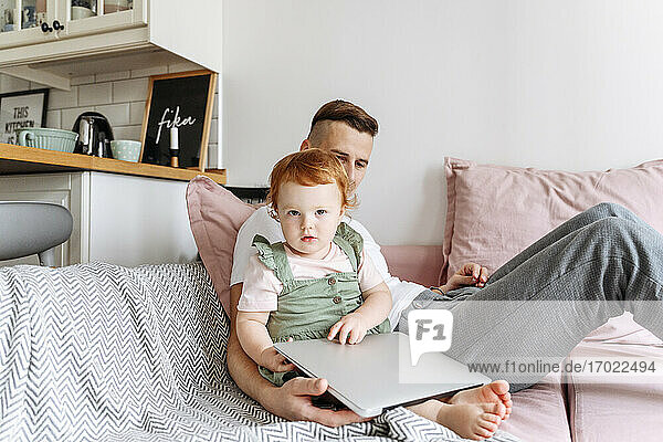 Mann mit kleiner Tochter auf Sofa mit Laptop