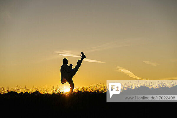 Silhouette of man practicing martial arts against setting sun