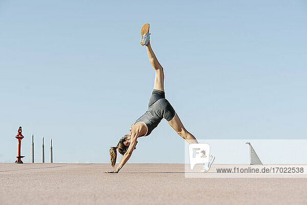 Mid adult sportswoman exercising yoga against clear sky