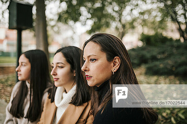 Thoughtful mother and daughters looking away while sitting in park