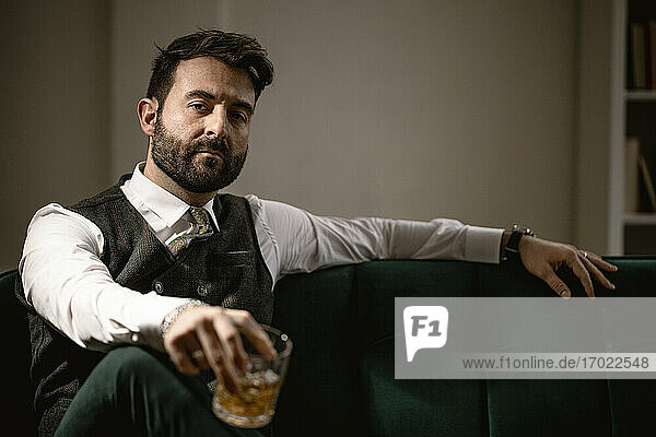 Porträt eines bärtigen Mannes auf dem Sofa sitzend mit einem Glas Whiskey in der Hand