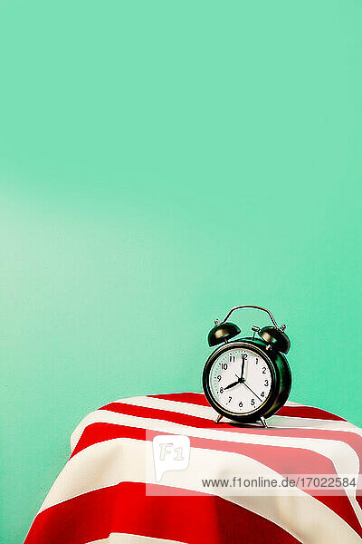 Studio shot of alarm clock standing on white and red striped pattern