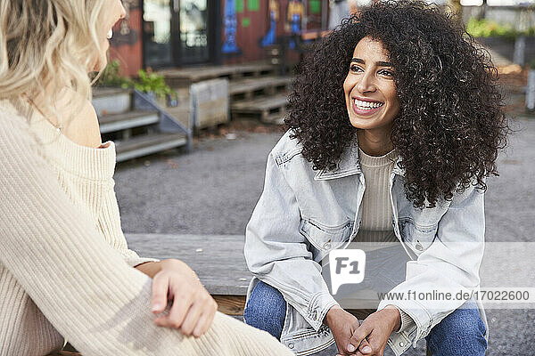 Smiling young woman looking at female friend while sitting on seat