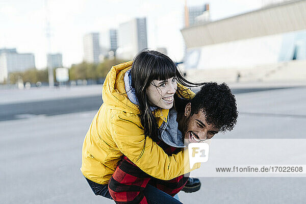 Playful man piggybacking cheerful friend while playing outdoors