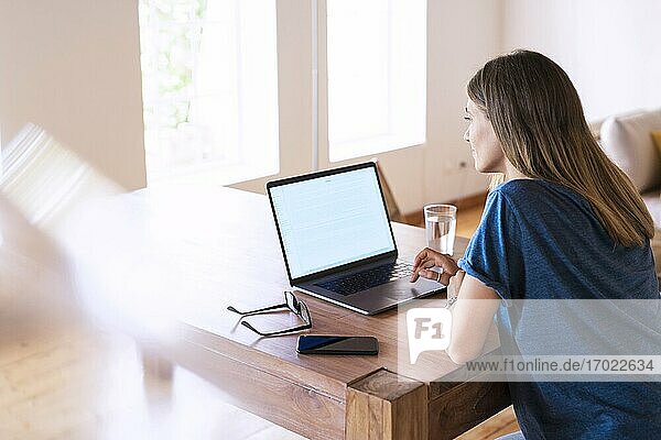 Brünette Geschäftsfrau mit Laptop am Tisch bei der Arbeit im Heimbüro