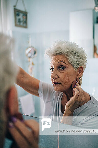 Ältere Frau schaut in den Spiegel  trägt Make-up auf