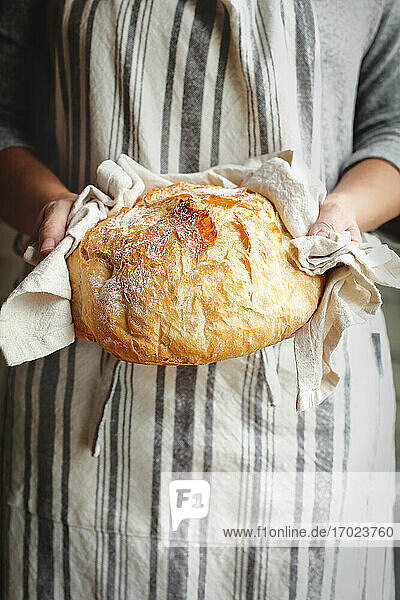 Woman wearing an apron holds freshly baked artisan bread in her hands
