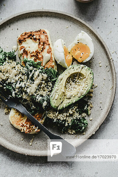 Millet with avocado kale egg and grilled halloumi topped with tahini sauce