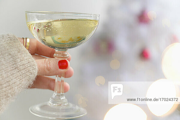 Hand holding champagne glass next to Christmas tree