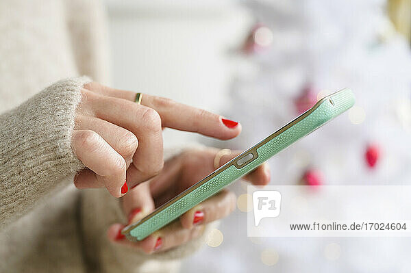Hände halten Smartphone neben dem Weihnachtsbaum